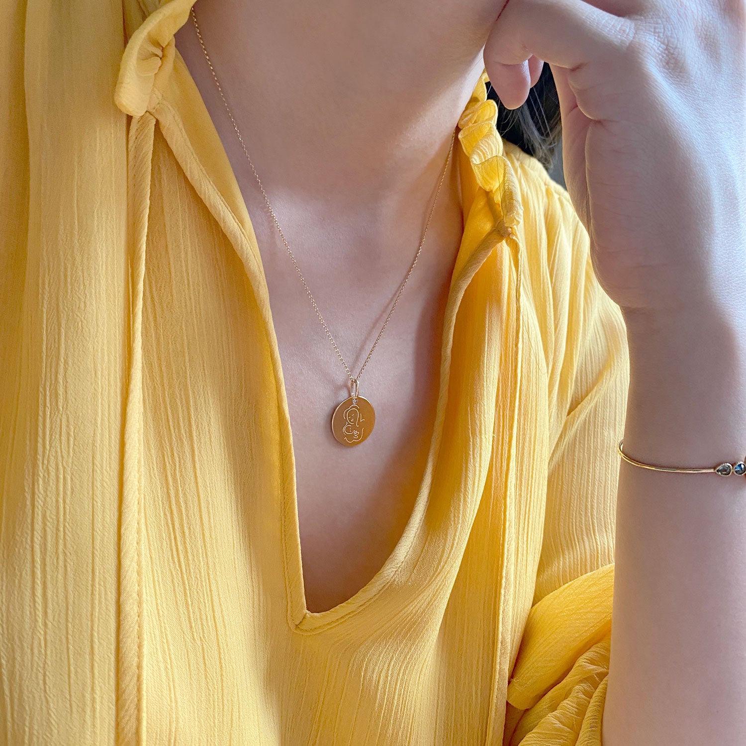 Muze 18k gold Vermeil Child Medal necklace on model with yellow dress , art inspired jewelry symbol of love, protection, tenderness and motherhood. A meaningful sentimental gift perfect for mother, newborn or godchild