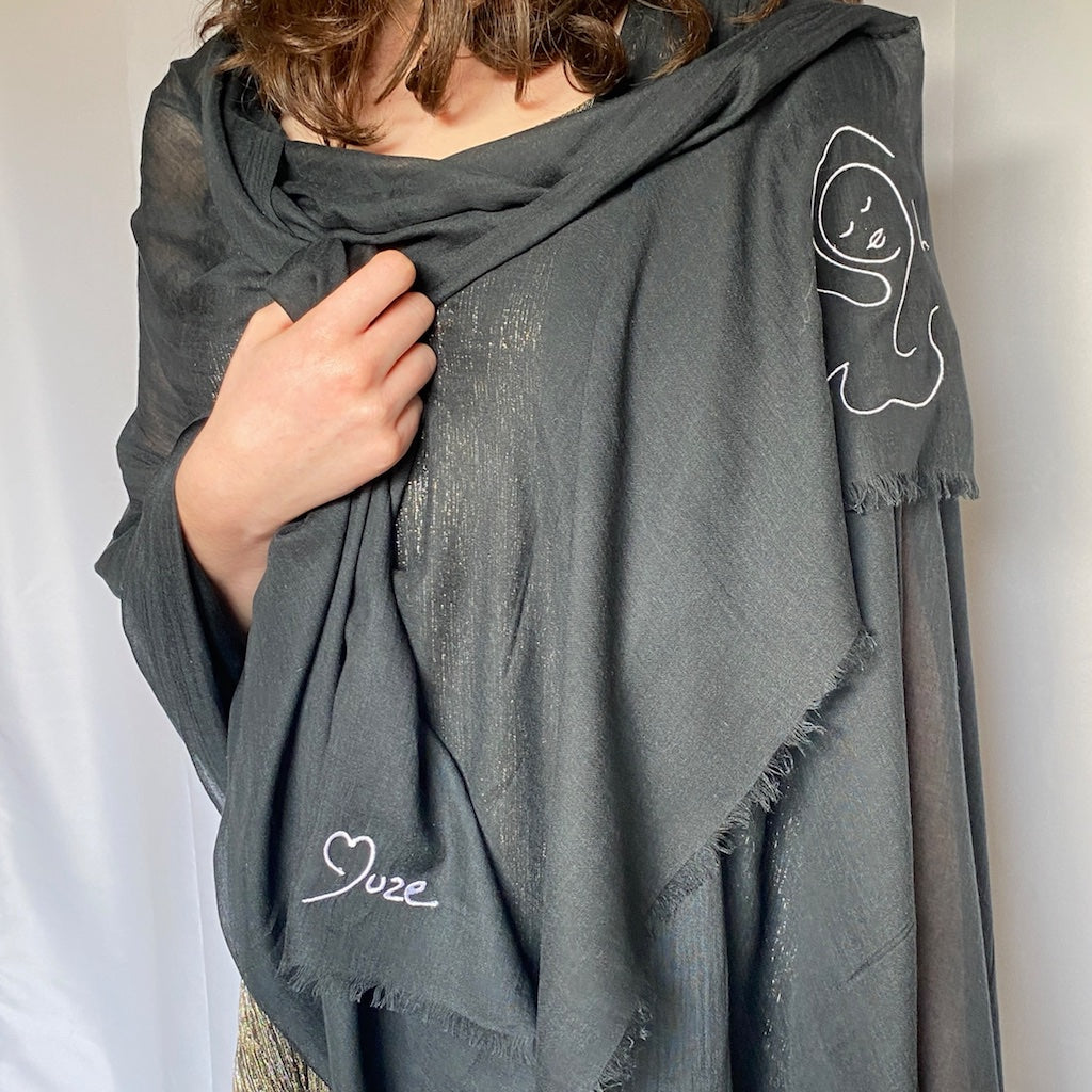 Muze black lightweight scarf in modal and silk on model shoulders displaying embroidery of a heart shape and muze logo