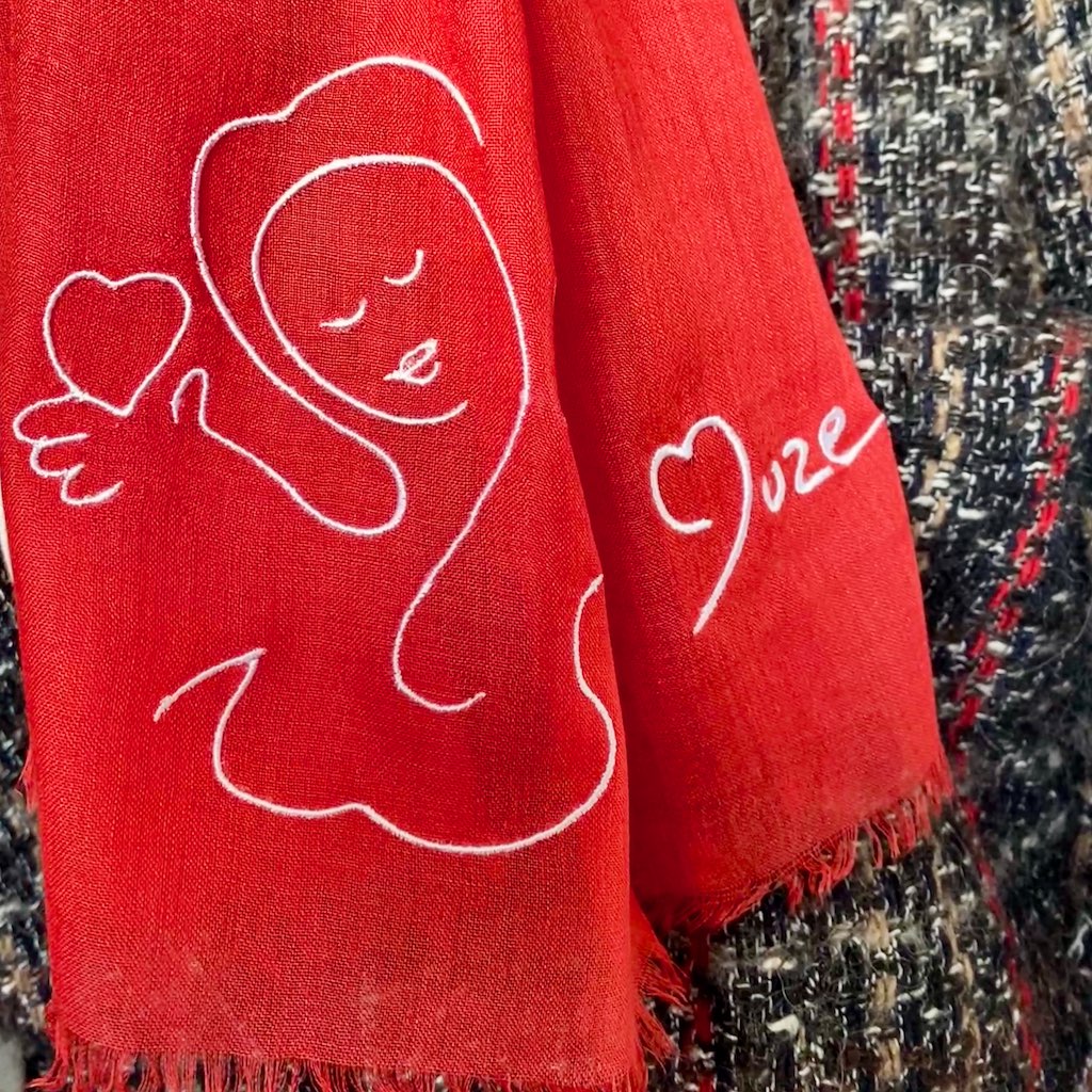 Love and Muze logo  : Muze red lightweight scarf in modal and silk on model displaying embroidery of love peace original artistic drawing on one side and Muze logo on other